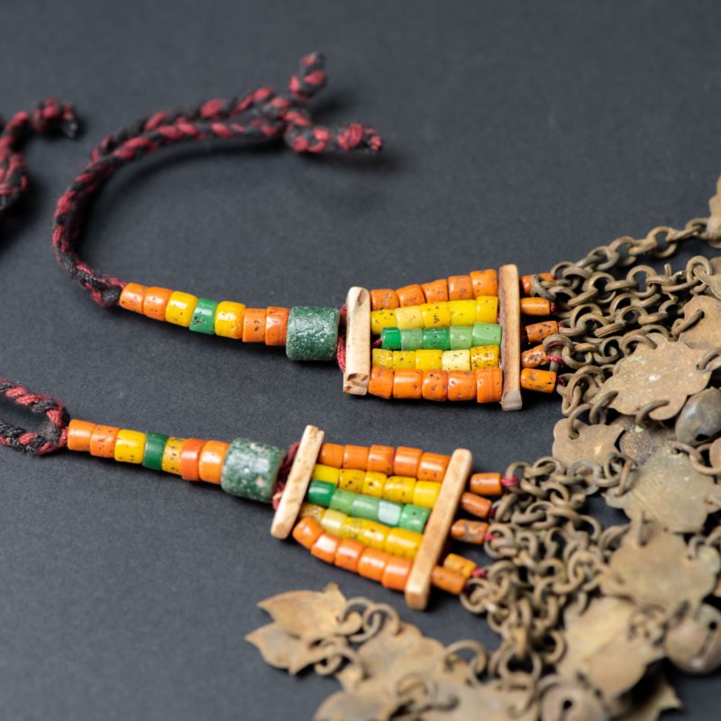 Pair of earrings from the Paiwan tribe, made of orange, yellow, and green beads, ending in six brass chains holding small bells and brass leaves.
