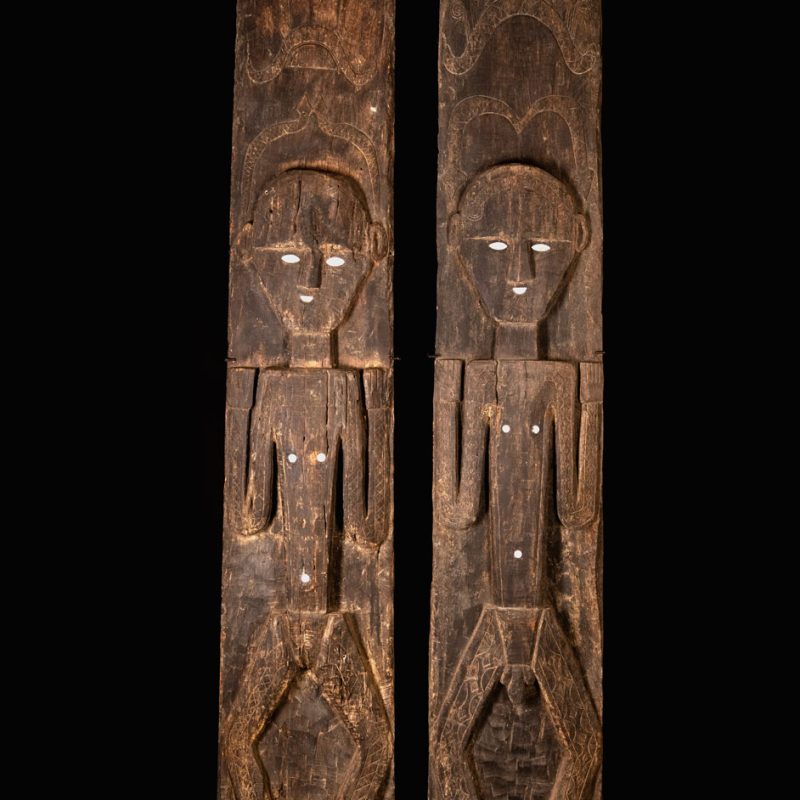 Pair of Paiwan Tribe Ancestor Panels, likely from Laiyi, carved with two figures—a male and a female. Their eyes, mouth, nipples, and navel are inlaid with porcelain. Their arms and legs are decorated with tribal motifs suggesting tattoos. Both figures wear hats, and the snakes carved above their heads indicate that they were important members of the nobility.