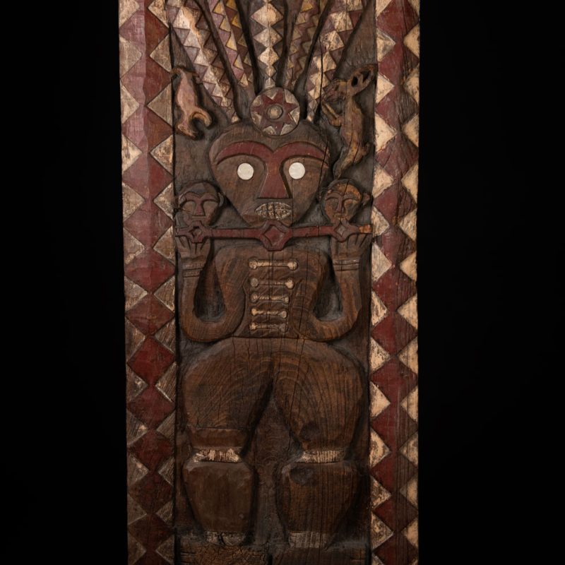 Panel from the Paiwan tribe depicting an ancestor in ceremonial attire, wearing a headdress adorned with eagle feathers. The panel is painted in red and white.