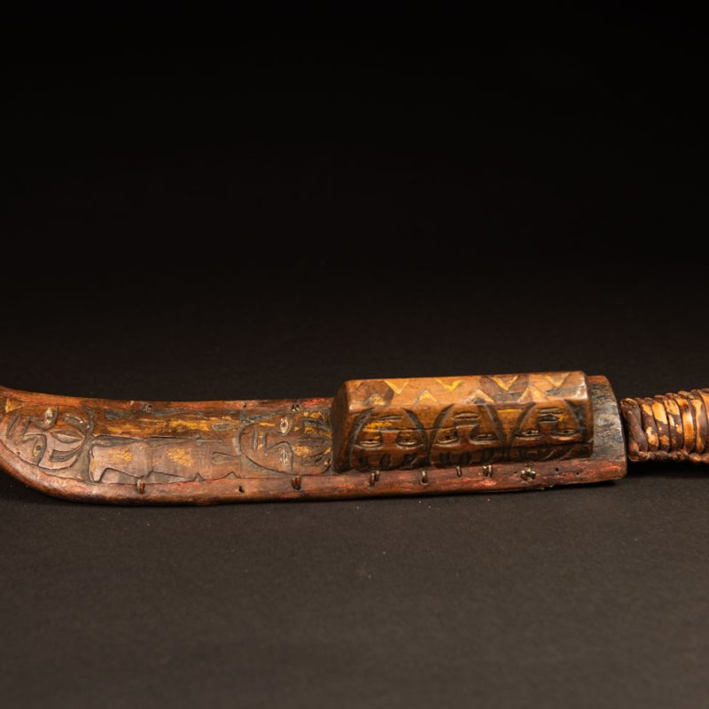 Sword from the Paiwan tribe, carved with stylized standing human figures, a serpent, and three faces. The blade and handle are forged from a single piece of iron.
