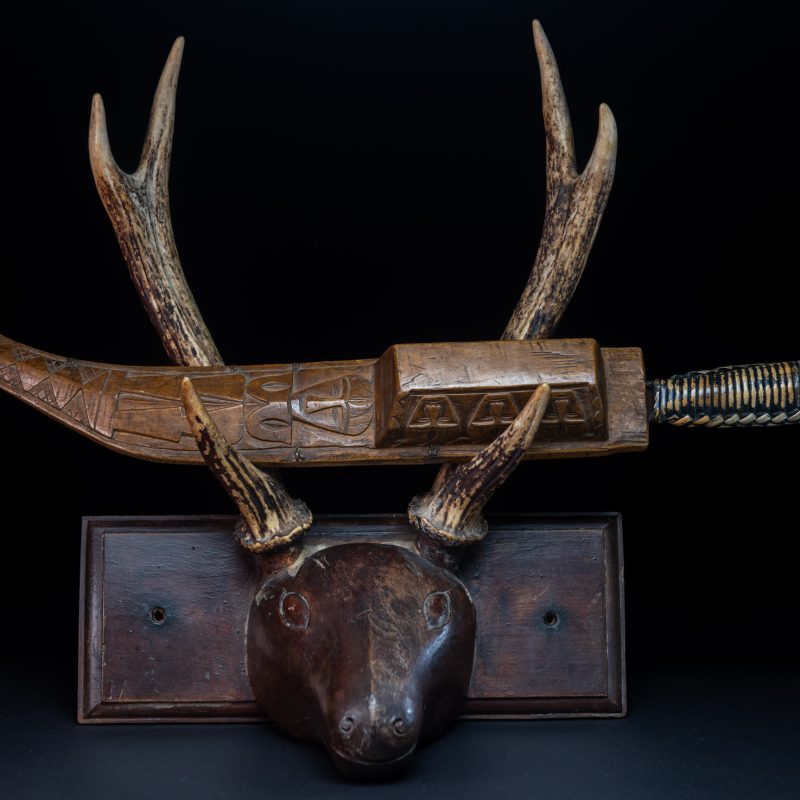 Short sword from the Paiwan tribe, with a sheath carved with a standing figure. The side of the sheath is adorned with three sculpted human heads. The sword is made in one piece with the handle, which is wrapped in rattan.