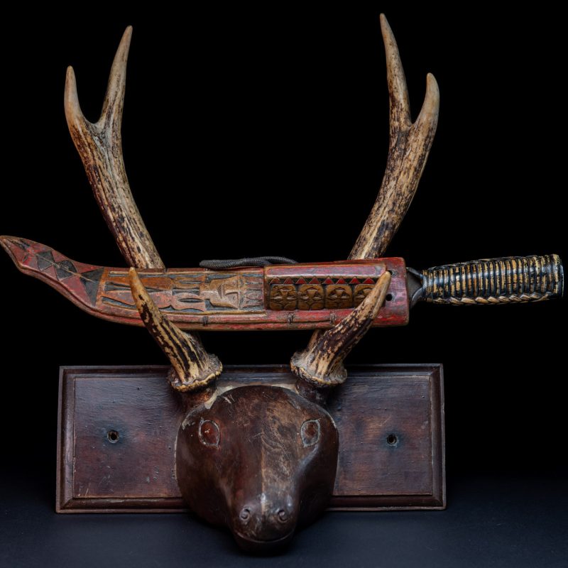 Paiwan tribe hunting knife with a sheath carved with a standing figure and painted in red. The blade and handle are forged as one piece, with the grip wrapped in rattan for protection.