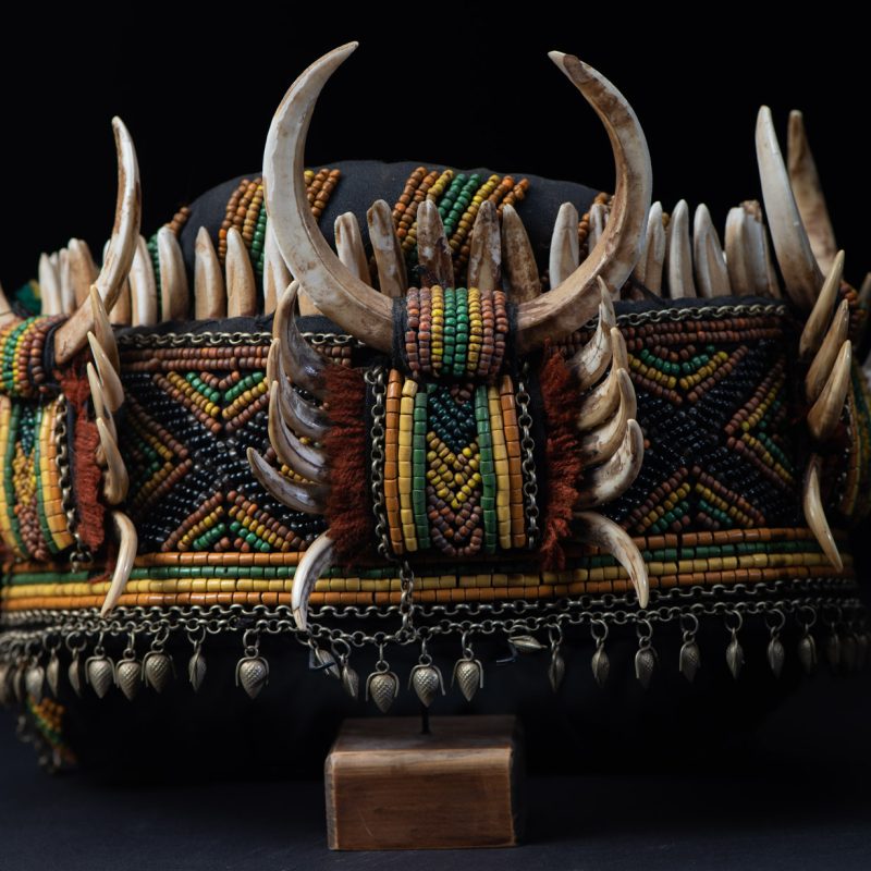 Women's headdress from the Paiwan tribe, made of green, yellow, red, and black beads arranged in geometric patterns, surrounded by chains and topped with boar tusks.